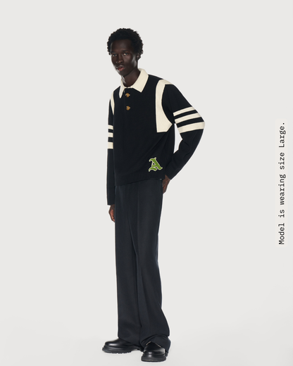 Man wearing a black rugby knit sweater with cream stripes and a green chenille logo. Aseye''s favorite sweater, the Kai Rugby Kni, was  inspired by the designer's brother, Kyrie Irving. 
