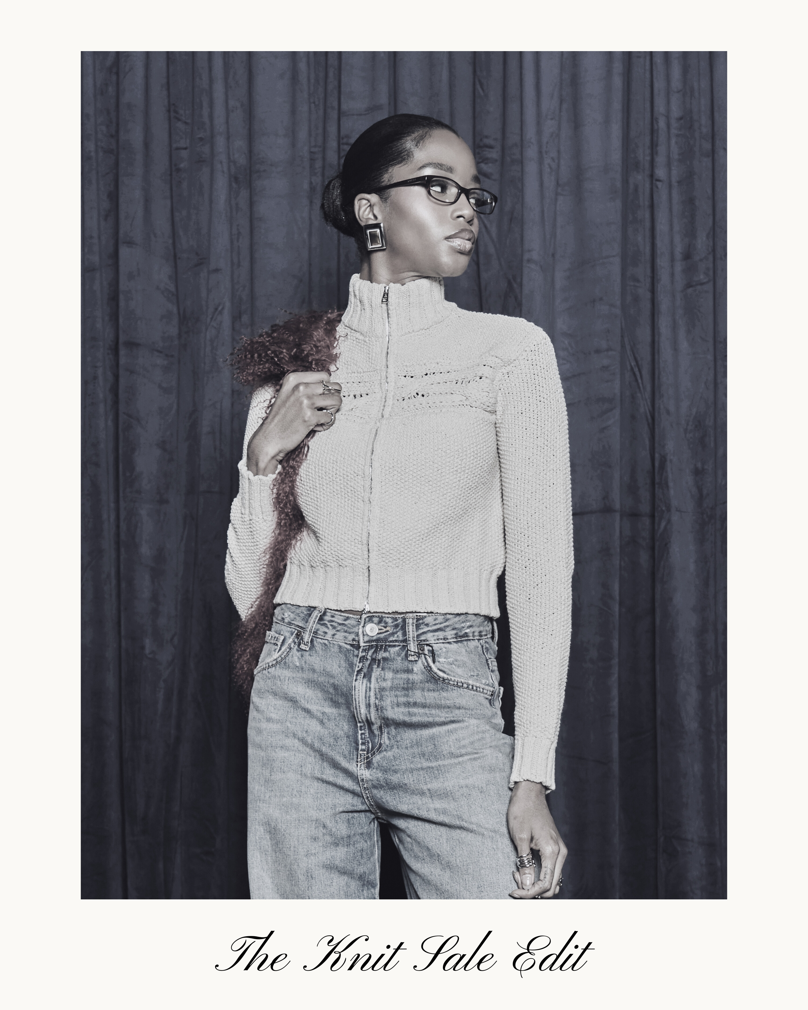 Woman wearing a light-colored Aseye knit sweater and jeans against a dark curtain background.