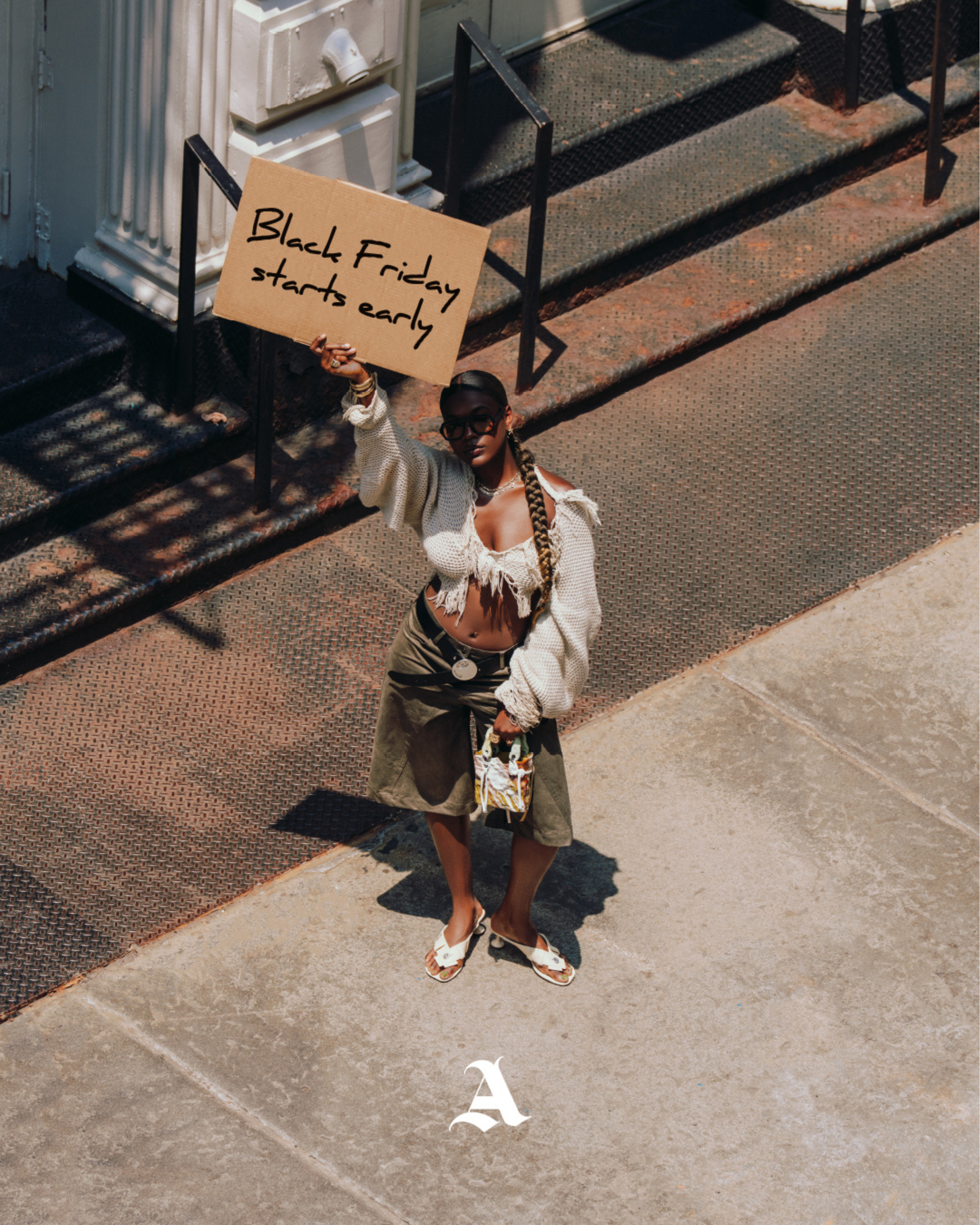Person holding a 'Black Friday starts early' sign on a city street. Model is wearing Aseye Studio jorts and knitwear. 
