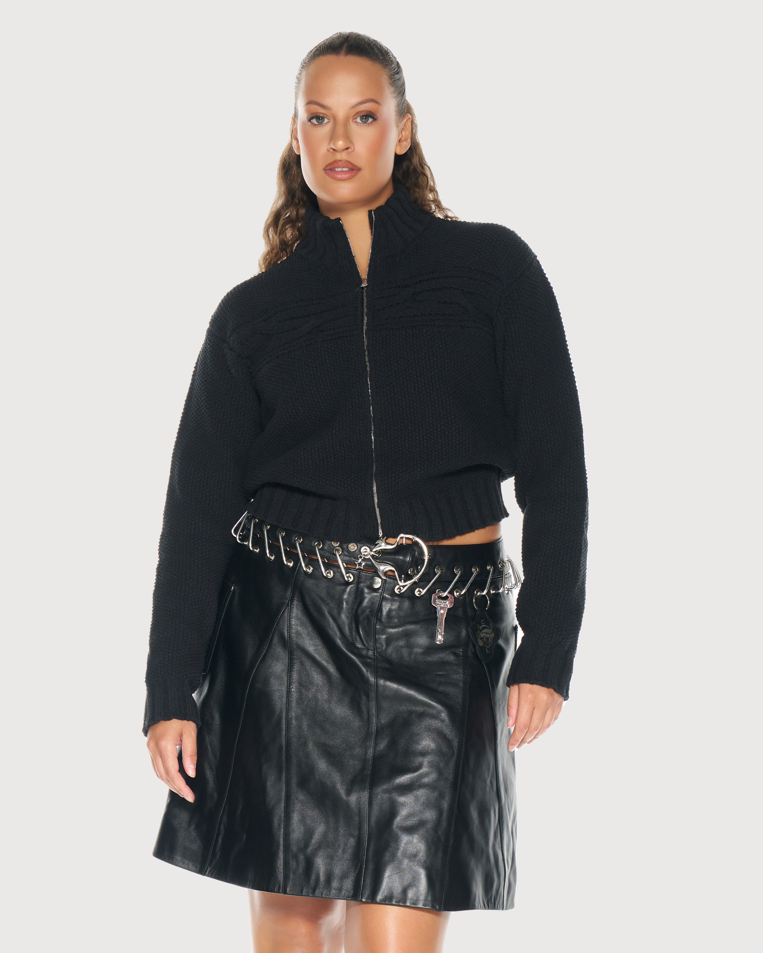 Woman wearing a black zip-up top by Aseye Studio  and black leather skirt on a white background