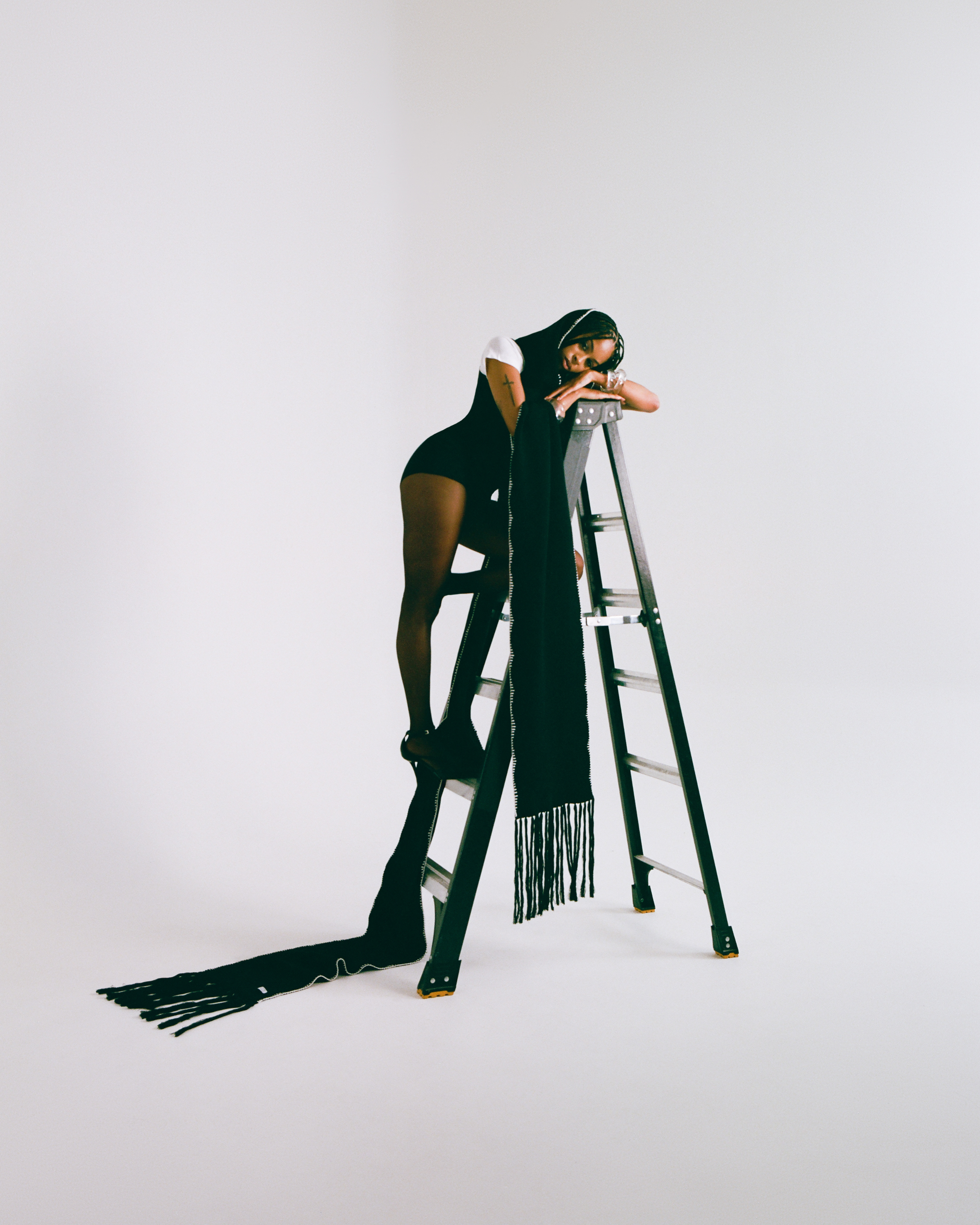 Person on a ladder with a long black scarf by Aseye Studio against a white background