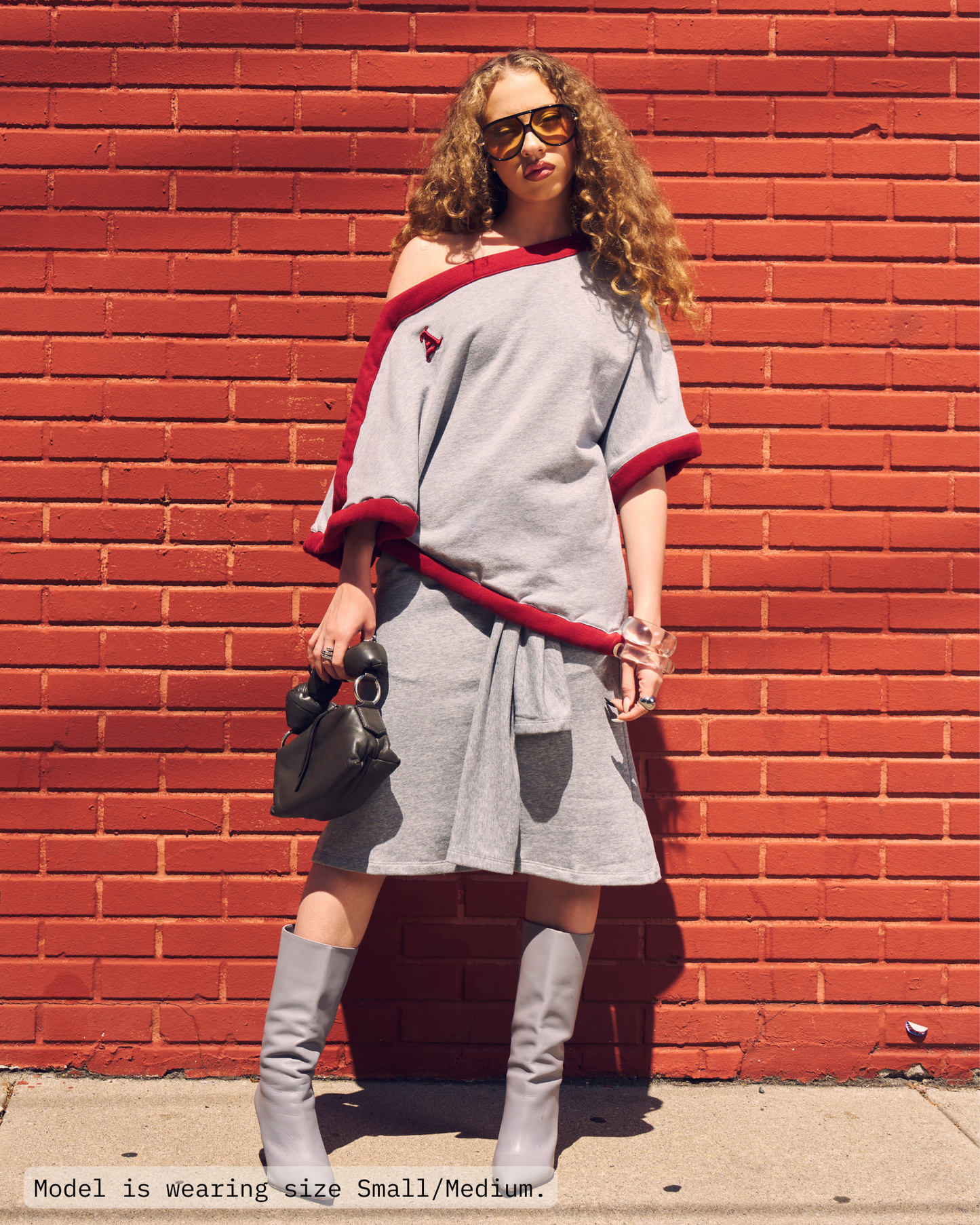 Woman is wearing a off-the-shoulder draped poncho top in heather grey with a deep red sporty border. Paired with heather grey french terry skirt and greay boots. Shop Jolie Draped Top on Aseye Studio