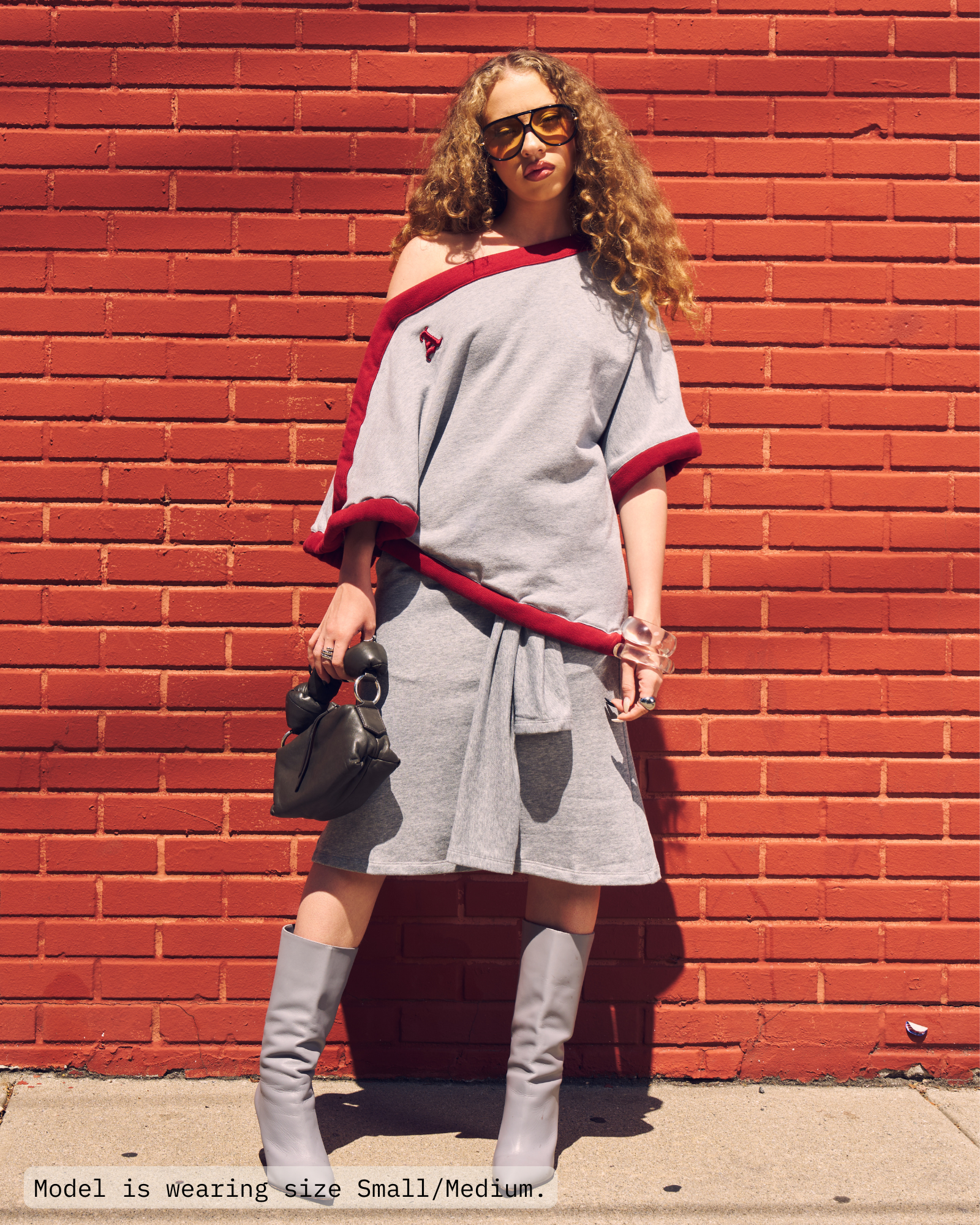 Woman is wearing a off-the-shoulder draped poncho top in heather grey with a deep red sporty border. Paired with heather grey french terry skirt and greay boots. Shop Jolie Draped Top on Aseye Studio