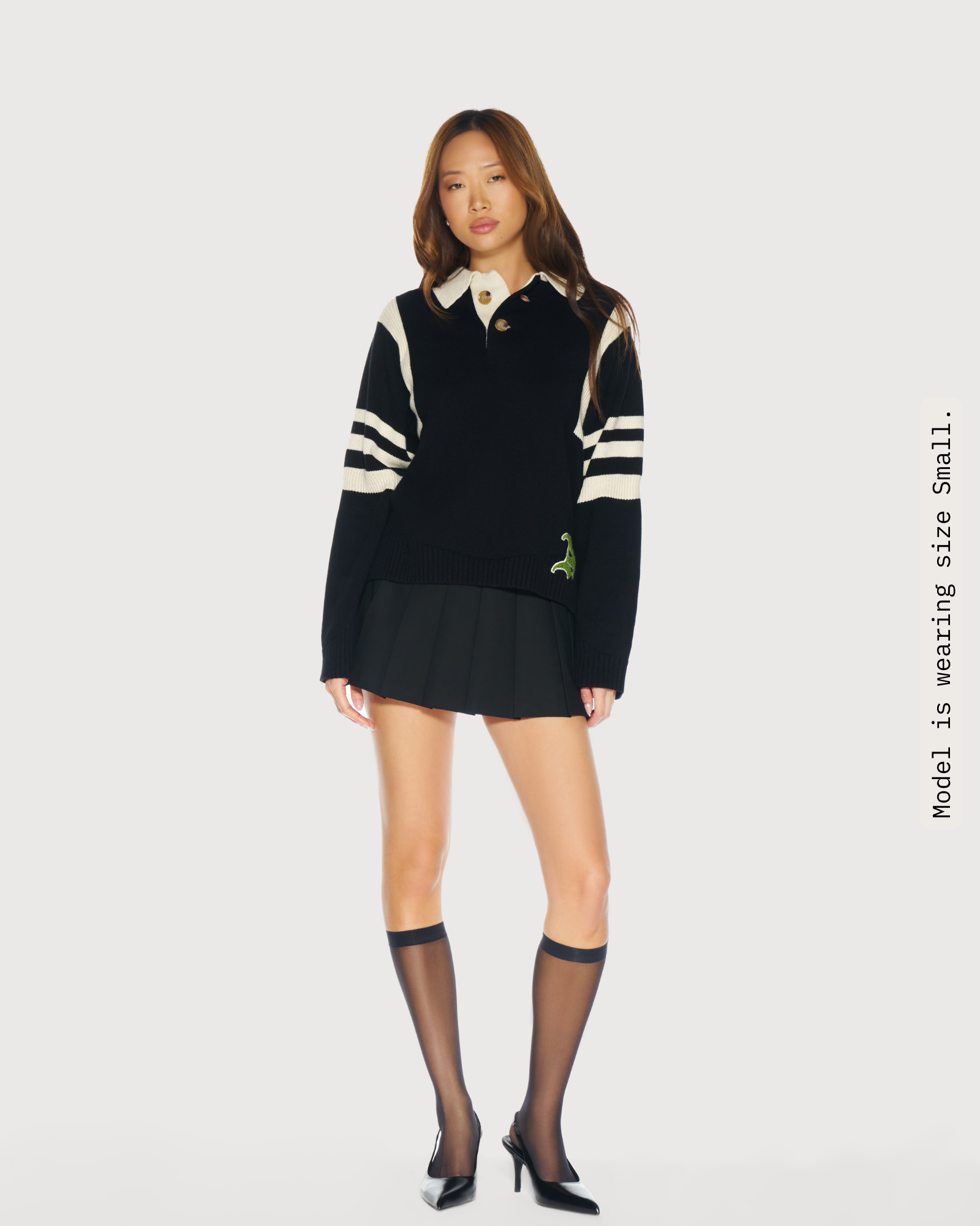 Woman wearing a black knit rugby sweater with cream stripes. Adorned with the  light green chenille logo on a white background. Elevated Unifrom for everyday. Aseye Studio