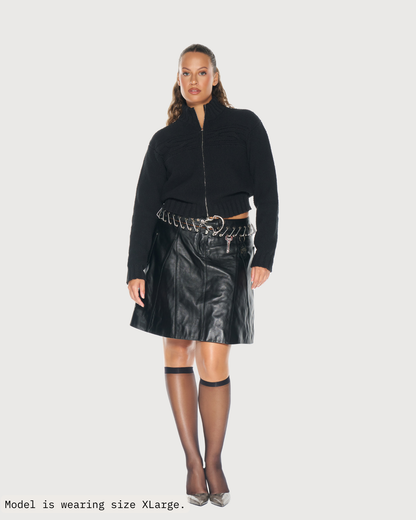 Woman wearing a black knit jacket by Aseye Studio and leather skirt on a white background. Tynia Knit Track Jacket