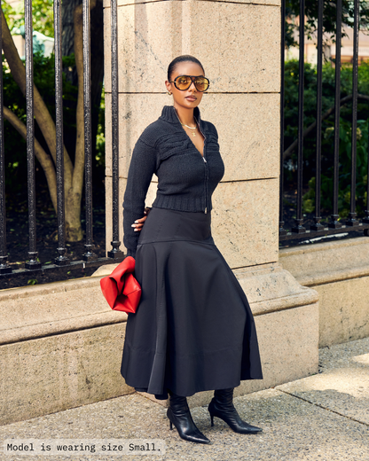 Woman in Aseye Studio Black Double-Zip Cardigan with cable knit and textured details. Paired with Black Long skirt and boots. 